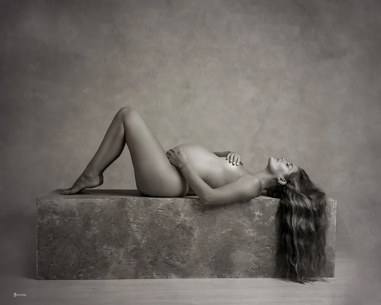 Fotografía de mujer embarazada en estudio de fotografía Chiclana tirada horizontalmente en una base de madera.
