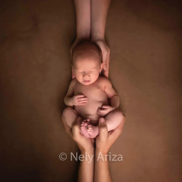 Fotografía de bebé recién nacido entre los brazos de sus padres.