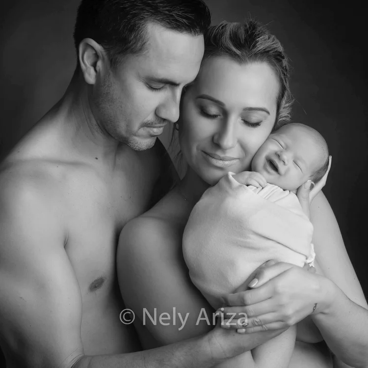 Fotografía de bebé recién nacido riéndose entre los brazos de sus padres.