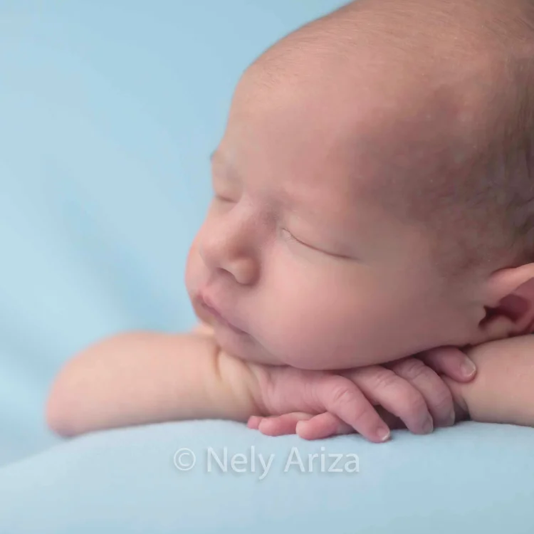 Fotografía de bebé recién nacido durmiendo sobre sus manitas.