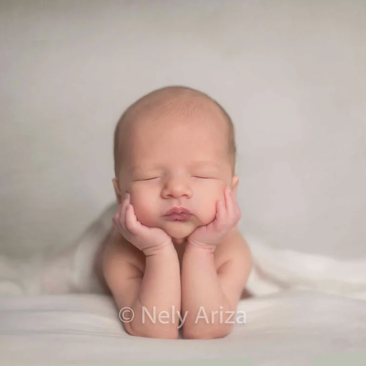 Foto de bebé recién nacido durmiendo sobre sus manos.