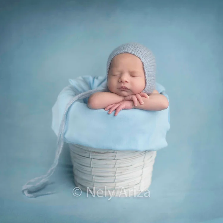 Fotografía de bebé recién nacido dentro de un cesta de mimbre.