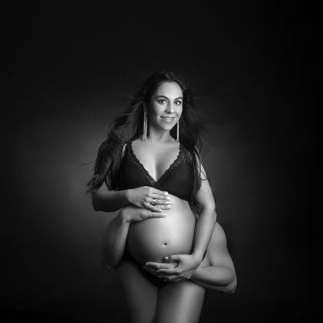 Fotografía de embarazada de 9 meses con las manos de su pareja